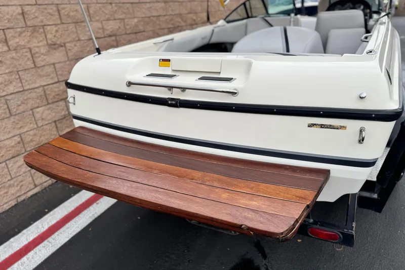 Slide: The Image of 1999 Malibu Sunsetter LX boat with wooden swim platform, parked near a brick wall. - 6