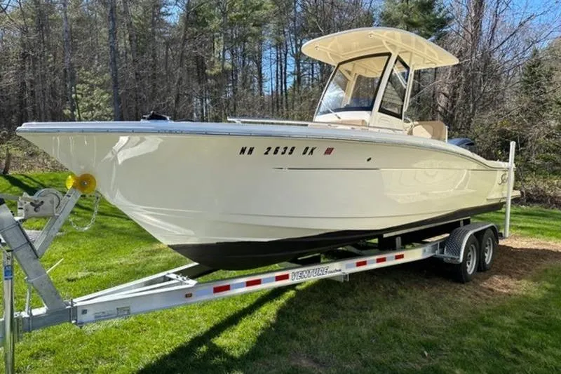 Slide: The Image of 2021 Scout 235 XSF boat on trailer, parked on grass with forest background. - 5