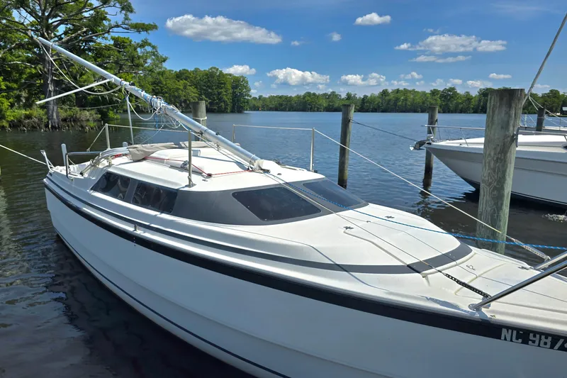 Slide: The Image of 2002 MacGregor 26X Powersailer docked on a serene lake under a clear blue sky. - 8
