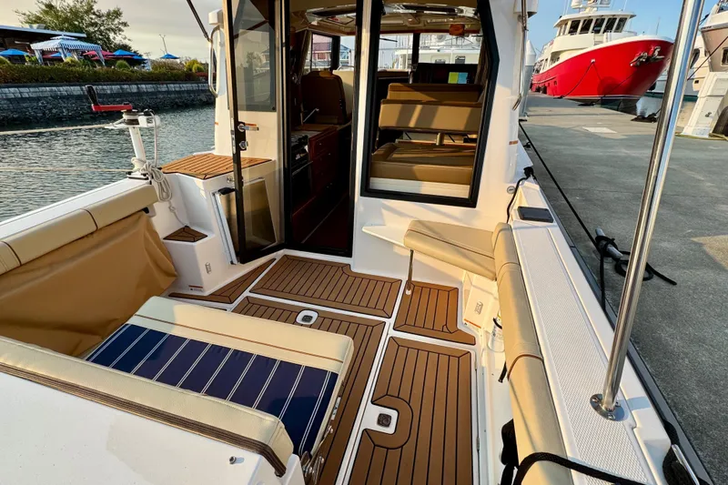 Slide: The Image of 2024 Ranger Tugs R-27 boat interior with seating and wood flooring at a marina. - 18