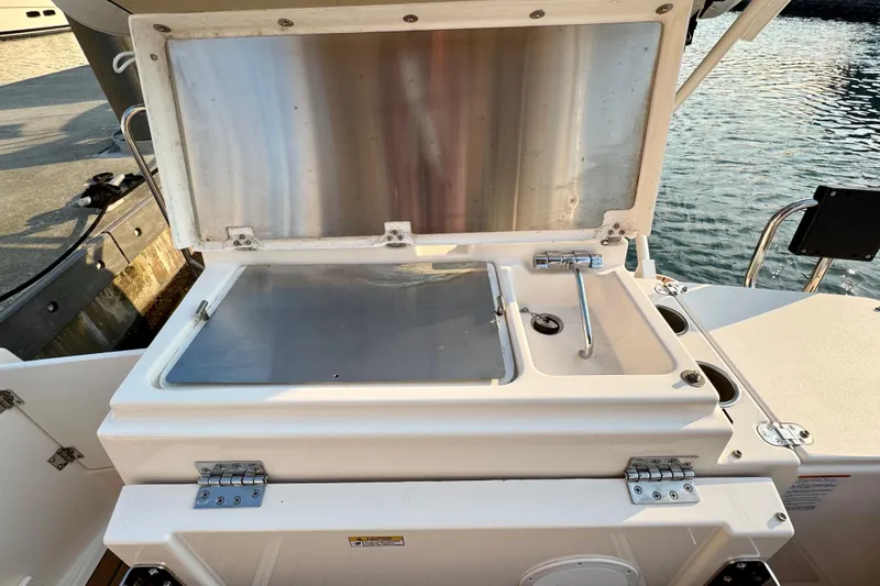 Slide: The Image of 2024 Ranger Tugs R-27 boat sink and storage compartment, open lid, dockside view. - 19