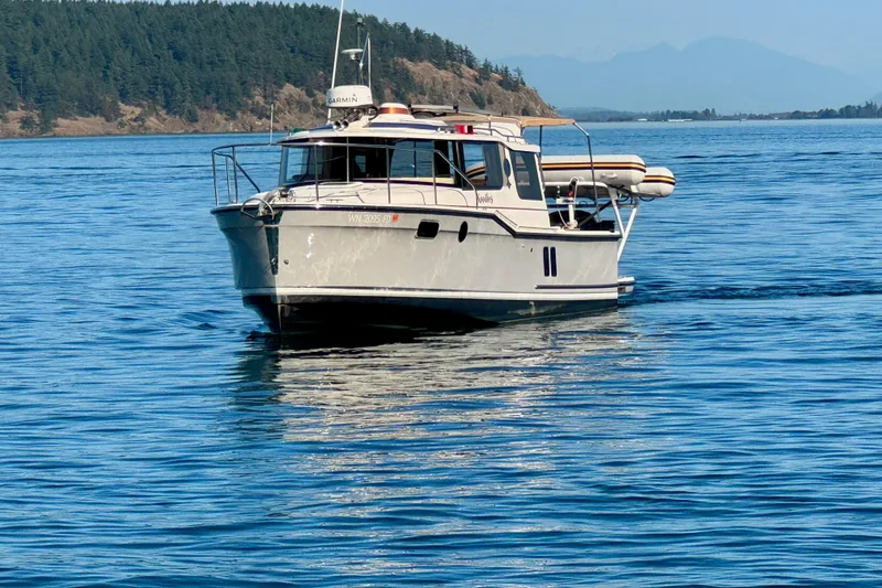 Slide: The Image of 2024 Ranger Tugs R-27 boat cruising on calm blue water near forested shoreline. - 23