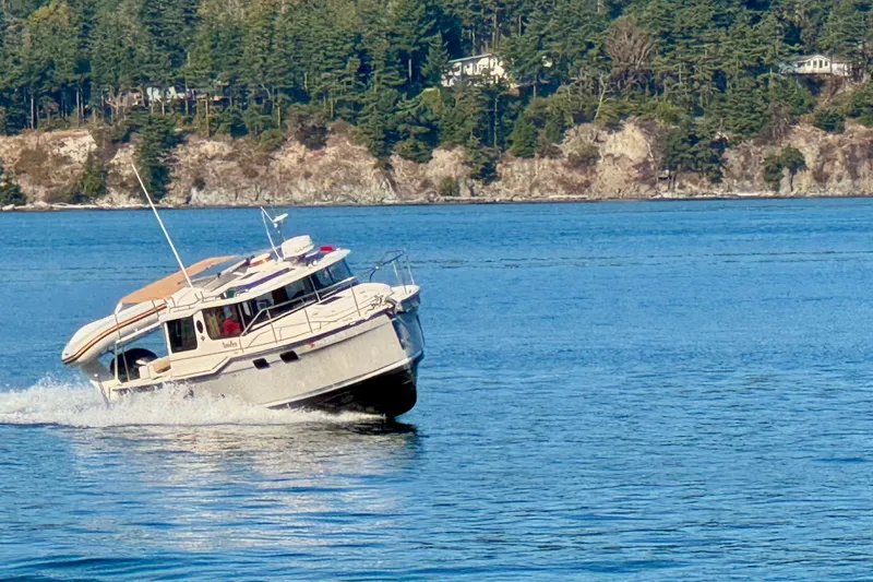 Slide: The Image of 2024 Ranger Tugs R-27 cruising on a scenic lake with forested shoreline. - 42
