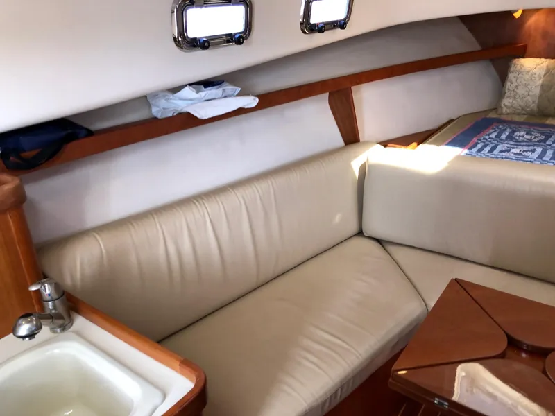 Slide: The Image of 2003 Mainship 30 Pilot II interior with beige seating, wooden accents, and small sink. - 26
