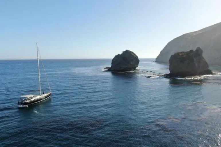 Slide: The Image of Sailing yacht Jeanneau 57 (2013) near rocky coastal landscape under clear blue sky. - 2