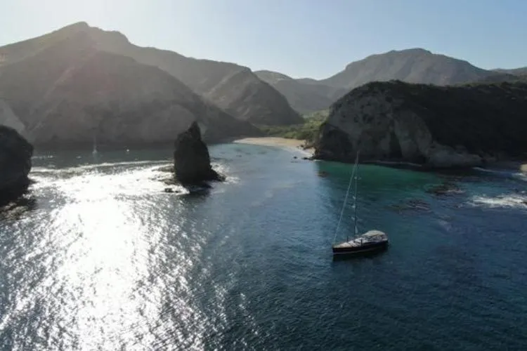 Slide: The Image of Sailboat Jeanneau 57 (2013) anchored in a scenic coastal bay with rocky cliffs. - 3