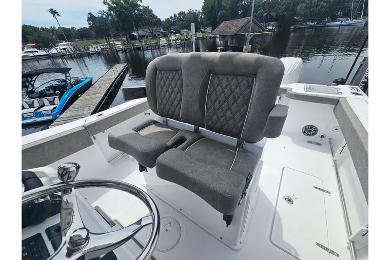 Slide: The Image of 2025 Sea Hunt Gamefish 27 Forward Seating with plush gray seats and steering wheel, docked by a lake. - 22