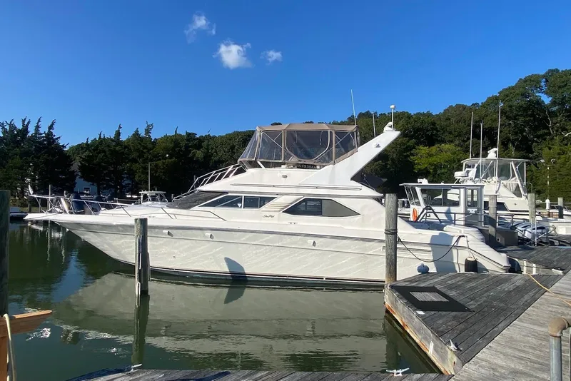 The Image of 1996 Sea Ray 440 Express Bridge yacht docked at marina under clear blue sky. - 0