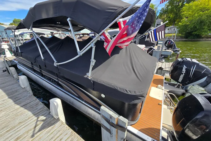 Slide: The Image of 2013 Premier 275 Boundary Waters pontoon boat docked with protective cover and American flags. - 3