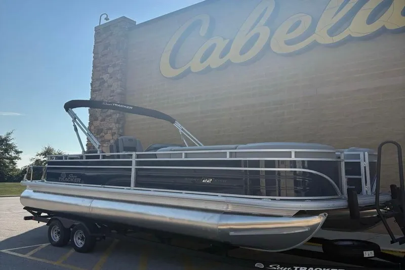 The Image of 2026 Sun Tracker SportFish 22 DLX pontoon boat parked outside Cabela's store. - 0
