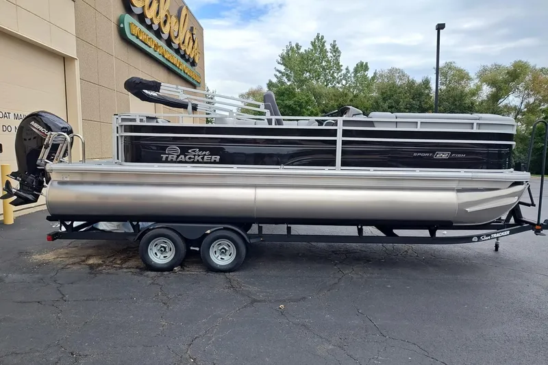 The Image of 2026 Sun Tracker SportFish 22 DLX pontoon boat on trailer outside Cabela's store. - 0