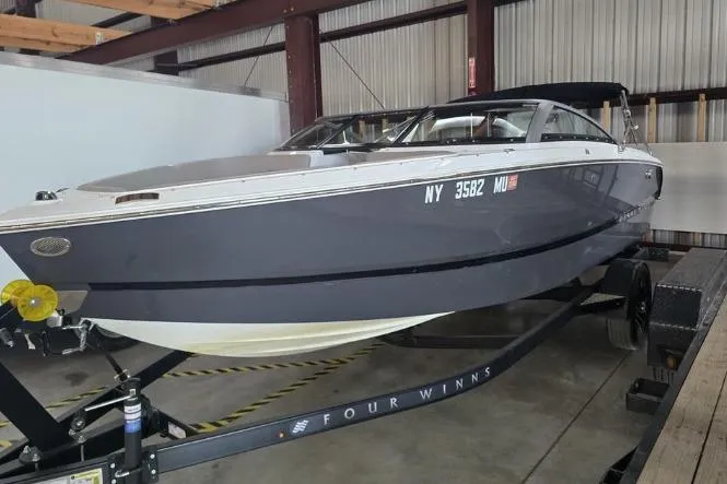 The Image of 2023 Four Winns H1 boat on trailer, parked against a green metal wall. - 0