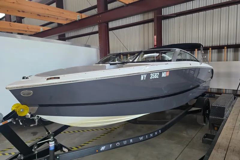 Slide: The Image of 2023 Four Winns H1 boat on trailer, parked against a green metal wall. - 1