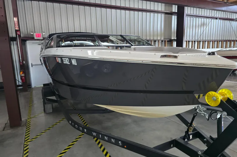 Slide: The Image of 2023 Four Winns H1 boat on trailer, parked outdoors near green building. - 2