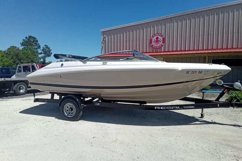 Slide: The Image of 2014 Regal 2000 Bowrider boat on trailer, parked outdoors under clear blue sky. - 3