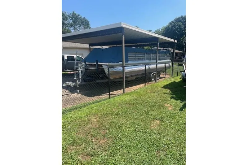 Slide: The Image of 2003 Godfrey SANPAN 2500 pontoon boat under a metal carport, surrounded by a fenced yard. - 34