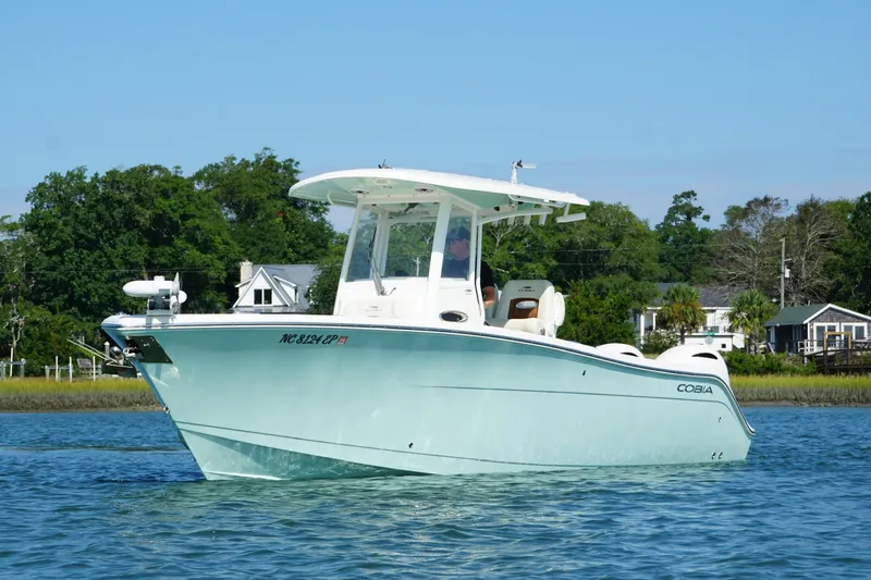 Slide: The Image of 2020 Cobia 280 Center Console boat on calm water, surrounded by lush greenery. - 2