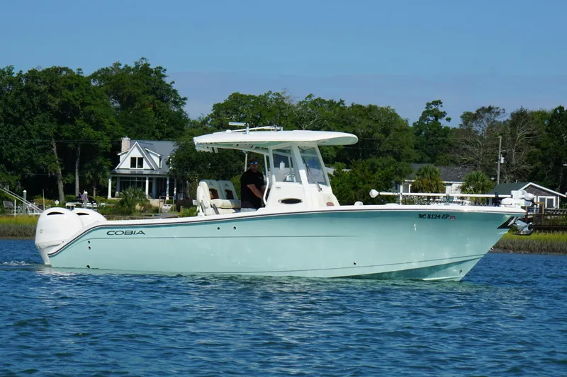 Slide: The Image of 2020 Cobia 280 Center Console boat cruising on a calm lake near shoreline homes. - 26