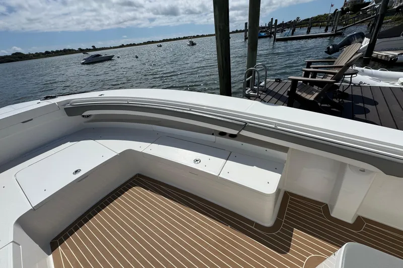 Slide: The Image of 2023 Regulator 34 Center Console boat interior with seating and wooden deck, docked by the water. - 17