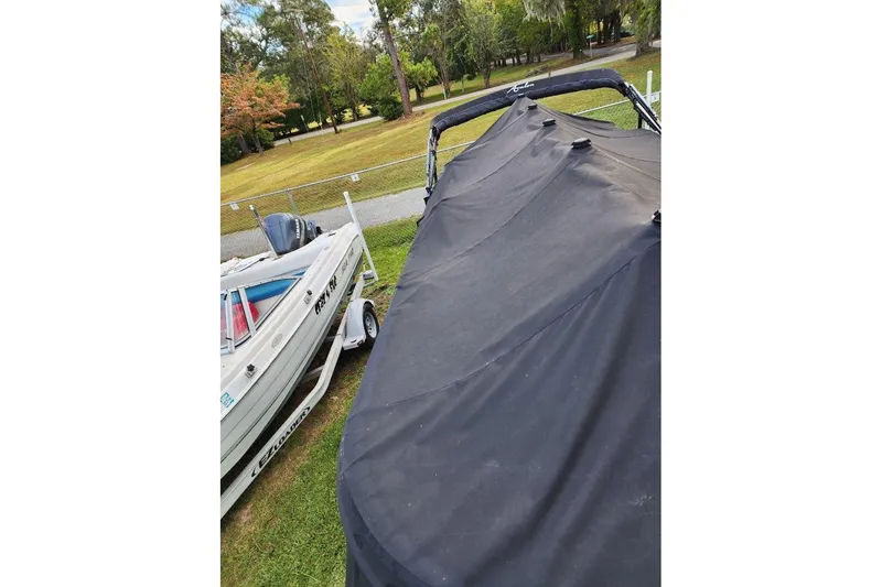 Slide: The Image of Covered Avalon GS Rear Fish 23' boat, 2022 model, parked on grass near another boat. - 20