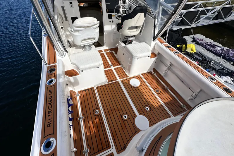 Slide: The Image of 2016 Sea Fox 256 Voyager boat interior with teak flooring and seating, docked by water. - 2