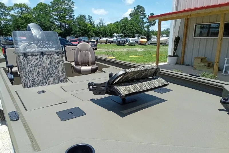 Slide: The Image of 2026 Thor 1900 Lake Hammer SC boat with camo seats and console, parked outdoors. - 8