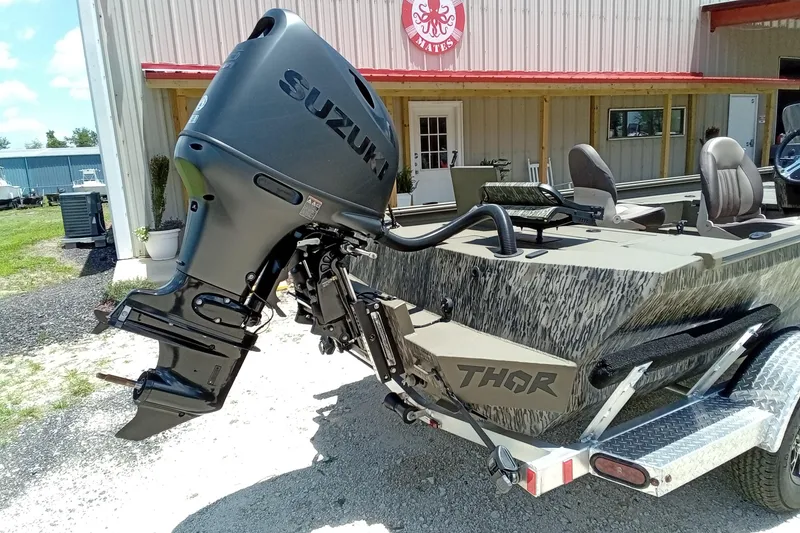 Slide: The Image of 2026 Thor 1900 Lake Hammer SC boat with Suzuki outboard motor, parked outside a building. - 15