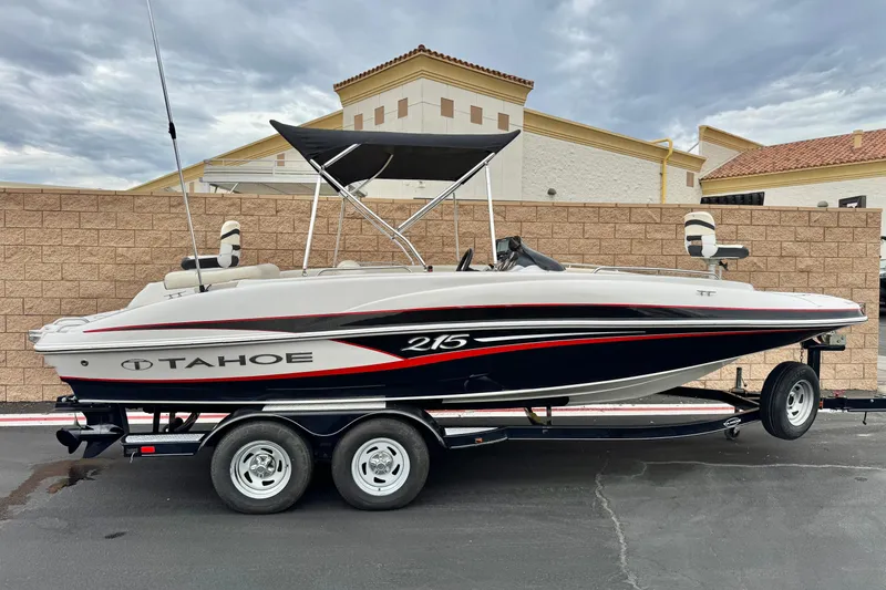 Slide: The Image of 2014 Tahoe 215 boat on trailer, parked outdoors with a brick wall backdrop. - 0