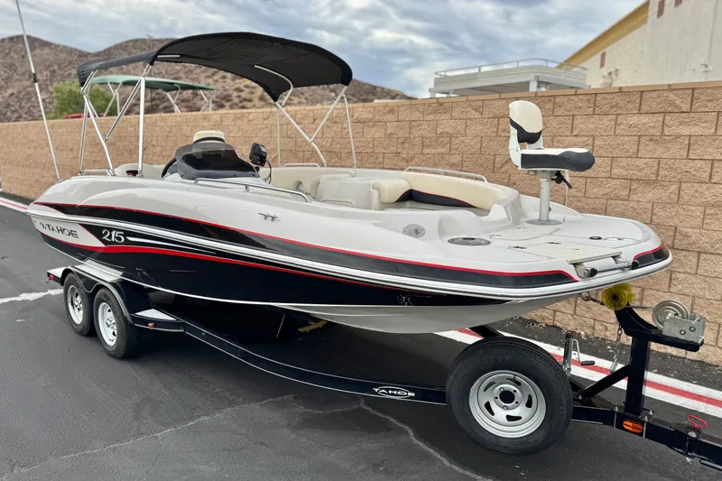 Slide: The Image of 2014 Tahoe 215 boat on trailer, parked near a brick wall, under a cloudy sky. - 1