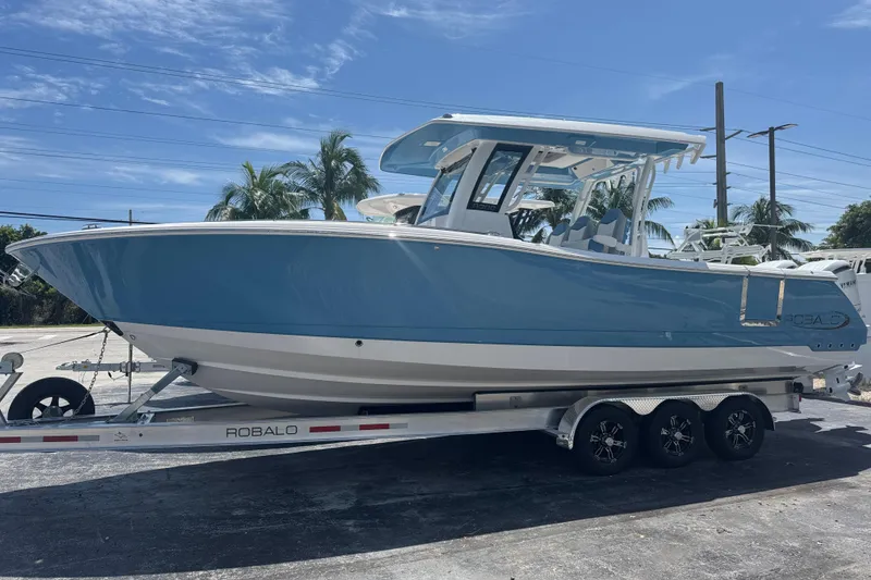 The Image of 2026 Robalo R300 Center Console boat on trailer, blue and white design. - 1