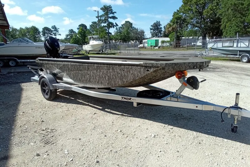Slide: The Image of 2026 Thor 1754 Timber Hammer boat on trailer, parked outdoors, surrounded by trees and other boats. - 6