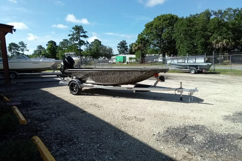 Slide: The Image of 2026 Thor 1754 Timber Hammer boat on trailer, parked outdoors, surrounded by trees and other boats. - 7