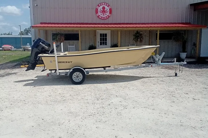 Slide: The Image of 2025 Fibercraft F16 boat on trailer with Suzuki outboard motor, parked outside a building. - 2