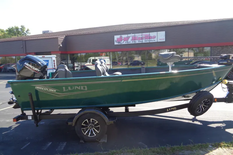Slide: The Image of 2026 Lund 1800 Explorer Tiller boat on trailer, parked outside a marine store. - 15