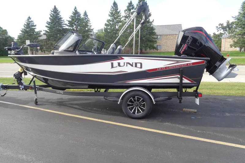 The Image of 2026 Lund 1875 Crossover XS boat on trailer, parked outdoors, side view. - 0
