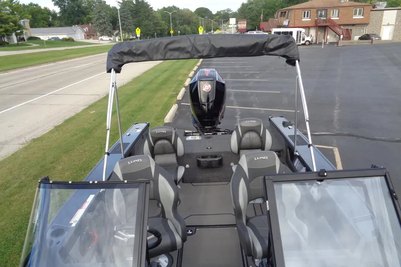 Slide: The Image of 2026 Lund 1875 Crossover XS boat interior with seating and outboard motor, parked on pavement. - 23