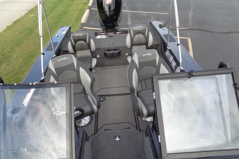 Slide: The Image of 2026 Lund 1875 Crossover XS boat interior with seating and windshield, parked on pavement. - 24