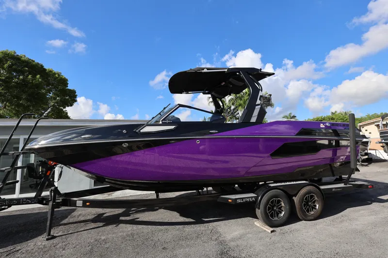 Slide: The Image of 2024 Supra SE550 boat in vibrant purple on trailer, under clear blue sky. - 2