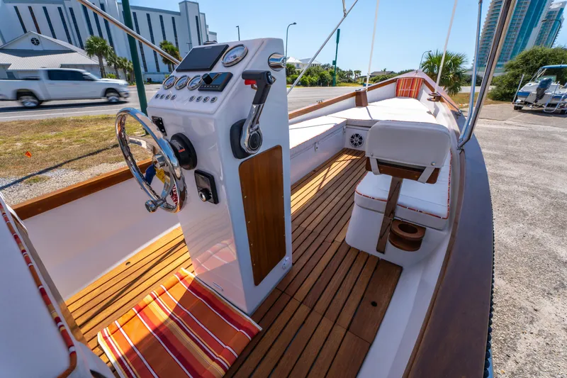 Slide: The Image of 2025 Caribiana Maracas 23 Skiff with wooden deck and modern controls, docked near a road. - 15