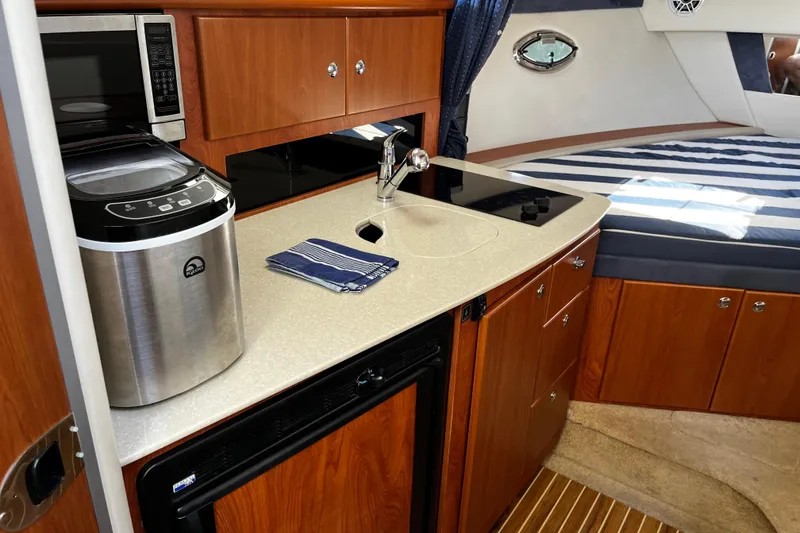 Slide: The Image of 2008 Bayliner 320 interior with kitchenette, featuring microwave, sink, and cozy sleeping area. - 9