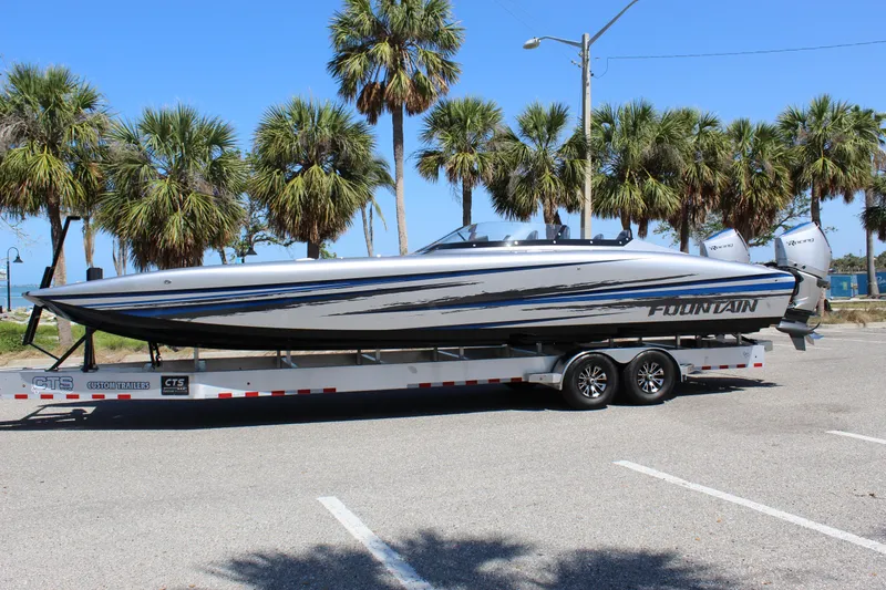 The Image of 2025 Fountain 34 Thundercat boat on trailer, parked near palm trees under clear blue sky. - 0