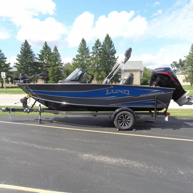 The Image of 2026 Lund 1875 Crossover XS boat on trailer, parked outdoors, sunny day. - 0