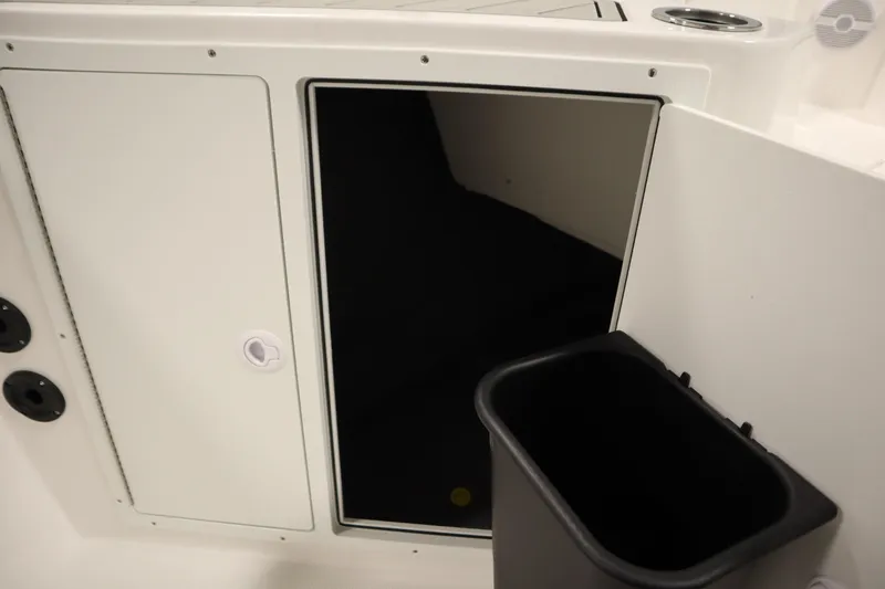 Slide: The Image of 2026 Yamaha Boats 220 FSH Sport storage compartment with open door and trash bin. - 19