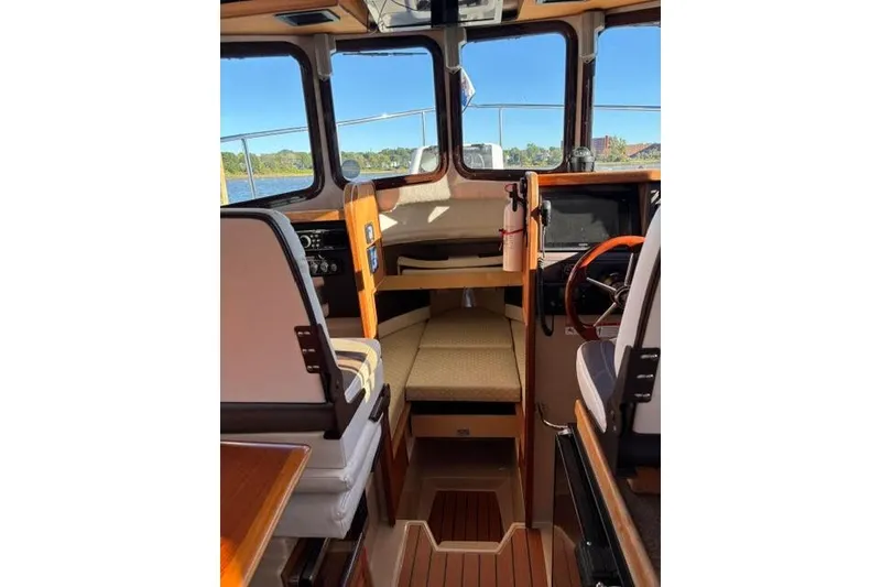 Slide: The Image of 2017 Ranger Tugs R-27 Tug interior with seating, steering wheel, and windows overlooking water. - 8