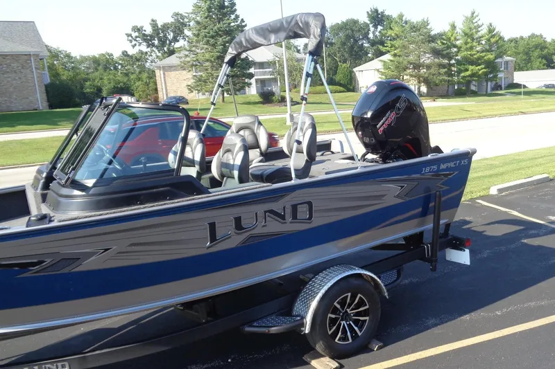 Slide: The Image of 2026 Lund 1875 Impact XS Sport boat on trailer, parked in residential area. - 2