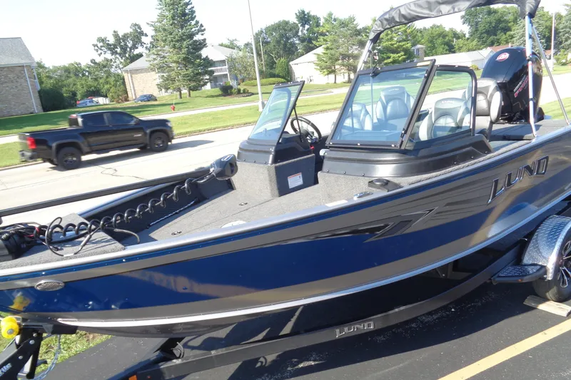 Slide: The Image of 2026 Lund 1875 Impact XS Sport boat, blue exterior, parked on a trailer in a suburban area. - 3