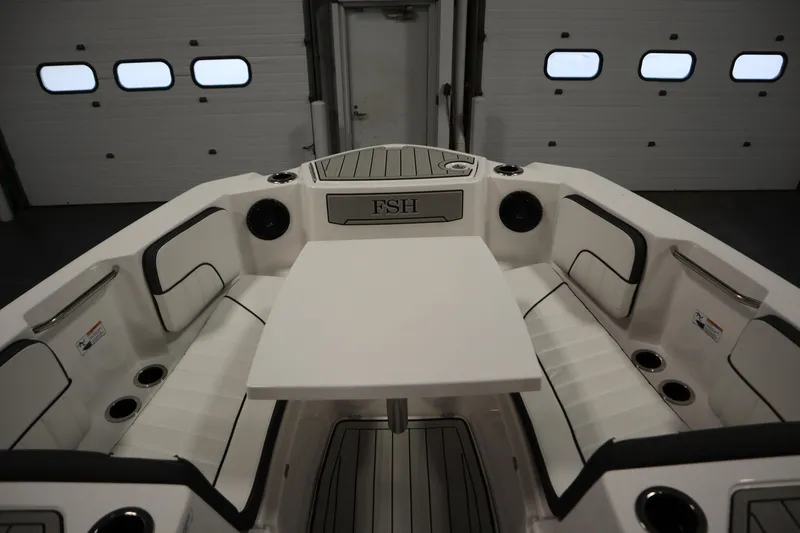 Slide: The Image of 2026 Yamaha Boats 222 FSH Sport E interior with seating and table in a garage setting. - 10