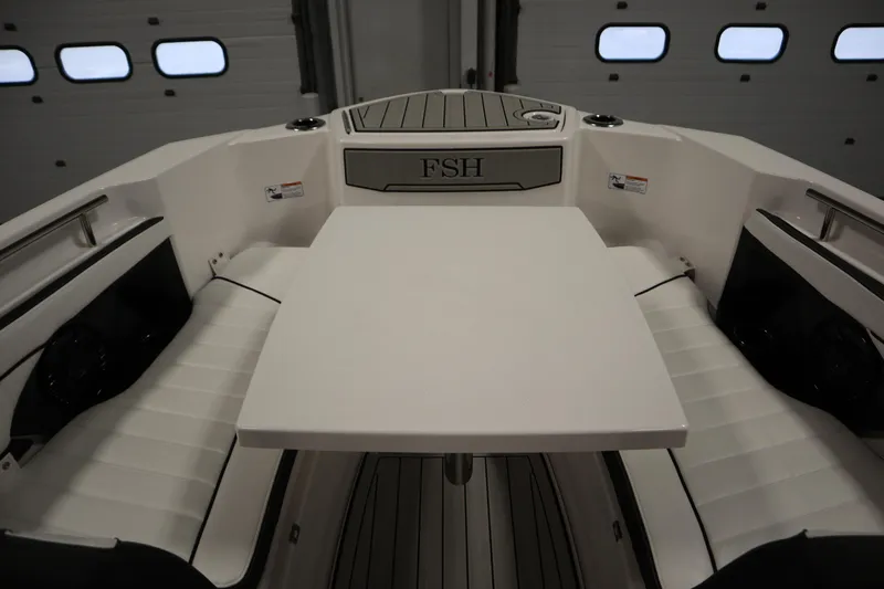 Slide: The Image of 2026 Yamaha Boats 255 FSH Sport E interior with seating and table in a garage setting. - 15