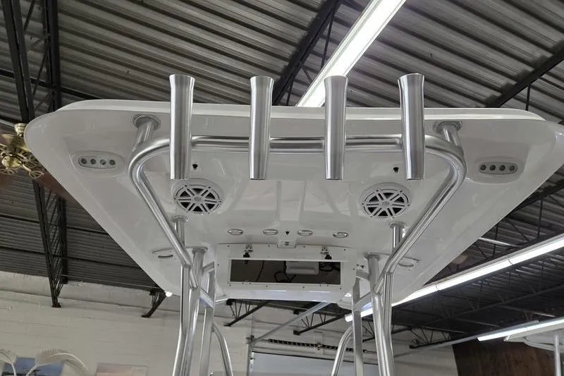 Slide: The Image of 2026 Sea Hunt Ultra 219 boat T-top with rod holders and speakers in a warehouse. - 8