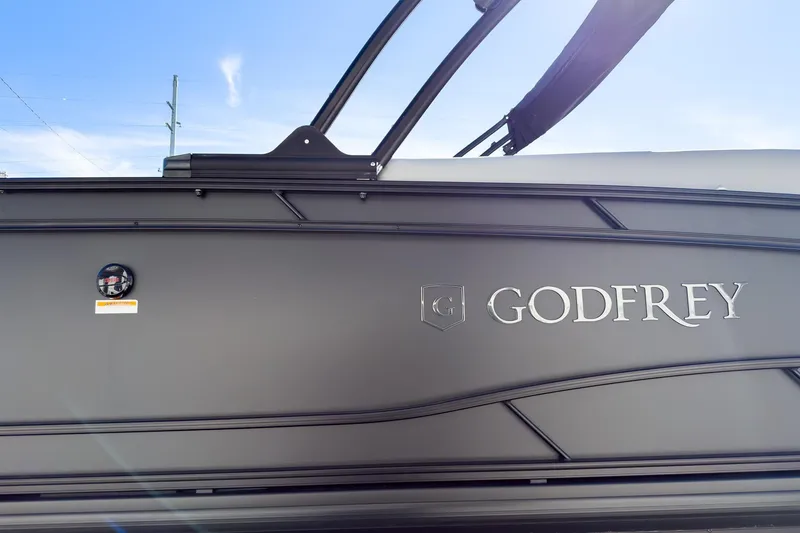 Slide: The Image of 2026 Godfrey Monaco 235 Split Bench boat side view with logo under blue sky. - 34